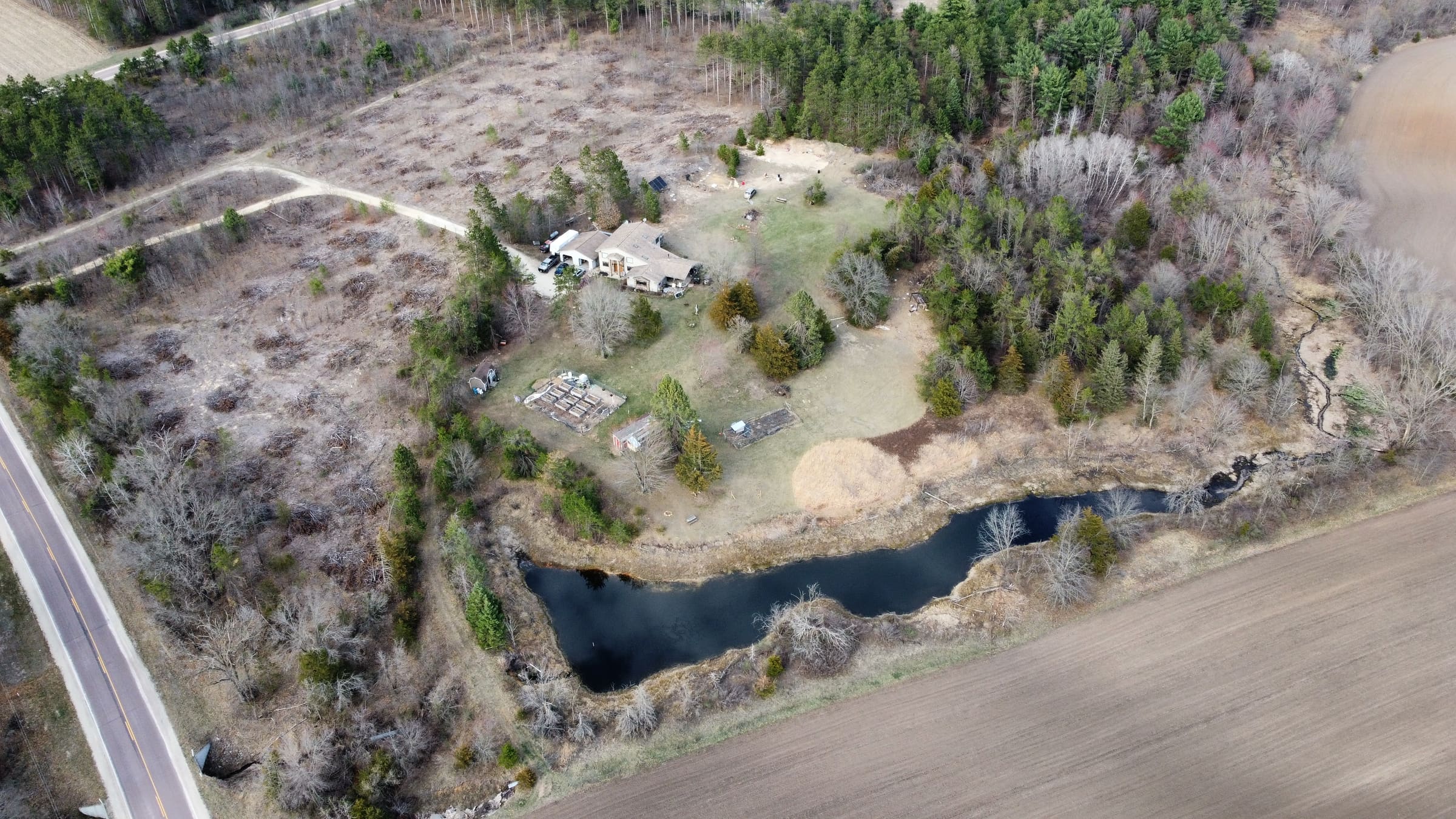 Aerial view of a home on wooded acreage with a pond, meadow and creek.