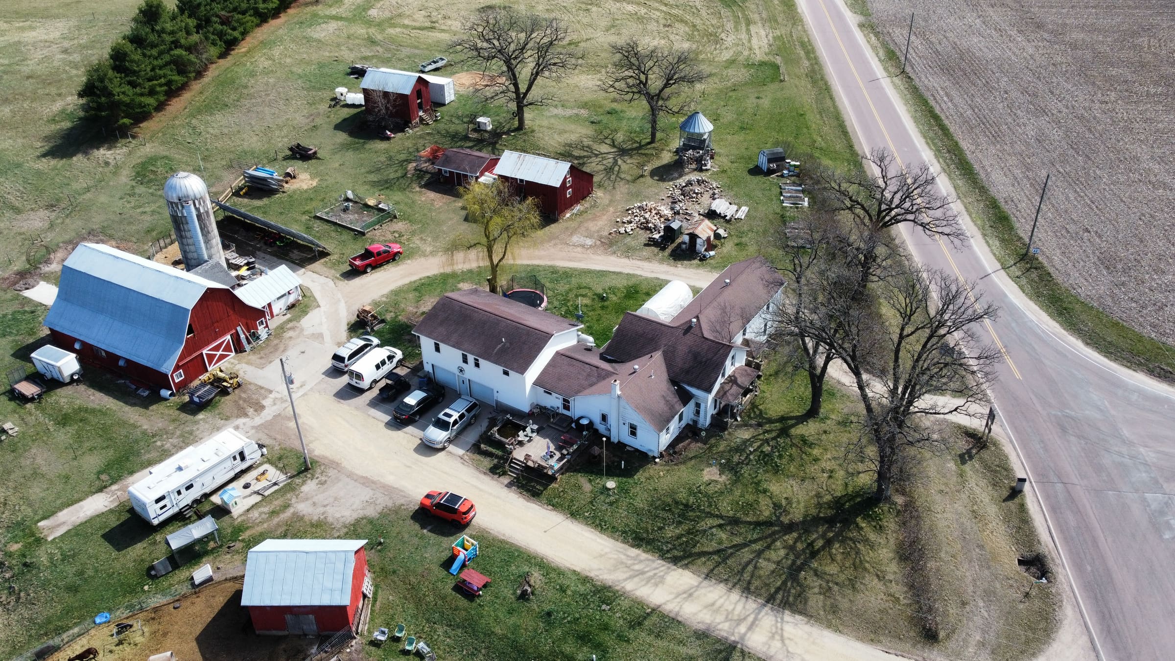 Aerial view looking down on a farmhouse, red barns, silo and outbuildings along a gravel drive.