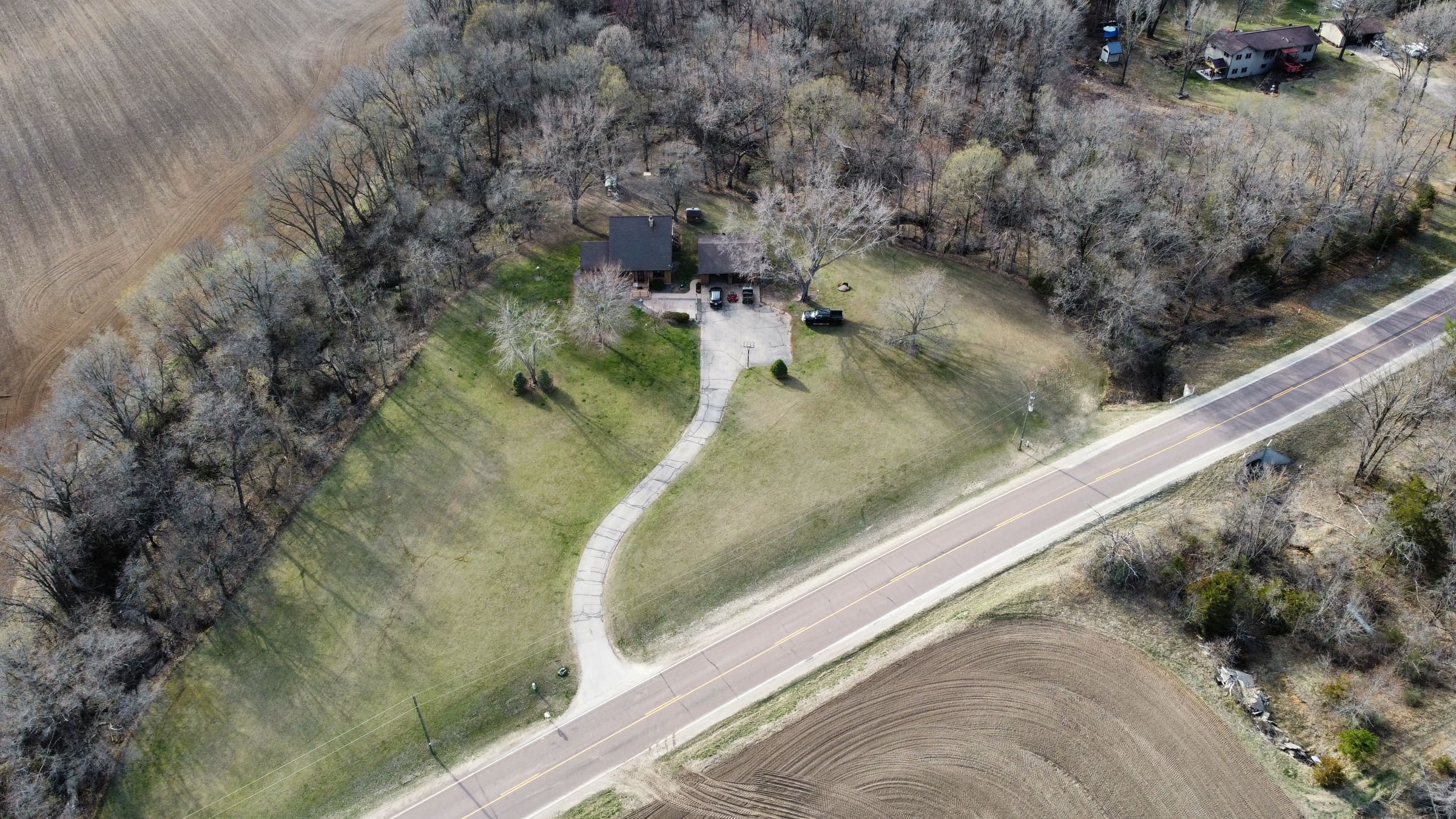 Aerial view of a house on a wooded lot with a long curved driveway leading to a country road.